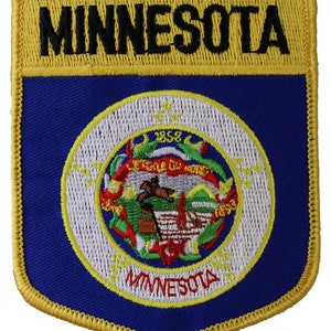 May include: A blue and gold embroidered patch featuring the state seal of Minnesota. The seal depicts a Native American man riding a horse, with the words "L'Etoile du Nord" and "1858" around the outer edge. The words "Minnesota" are embroidered in yellow below the seal.