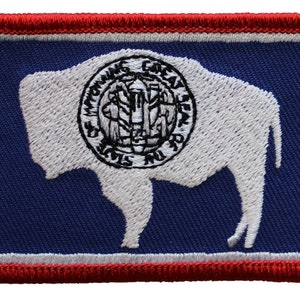 May include: Embroidered patch featuring the state flag of Wyoming. The patch is blue with a white outline and a red border. The flag depicts a white buffalo with the state seal on its back.