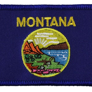 May include: A blue embroidered patch with the state seal of Montana. The seal features a mountain range, a river, and a sun with rays. The words "MONTANA" are embroidered in yellow above the seal.