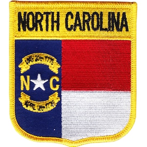 May include: A yellow embroidered patch with the words "NORTH CAROLINA" at the top and the state flag in the center. The flag features a blue field with a white star in the center of a white circle surrounded by a yellow wreath. The circle has the letters "N" and "C" on either side of the star. The flag is divided horizontally with a red stripe above a white stripe.