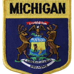 May include: A blue and gold embroidered patch with the state seal of Michigan. The seal features a shield with a sunrise over a lake, two elk, and the Latin phrase "Tuebor." The words "Michigan" and "E Pluribus Unum" are also embroidered on the patch.