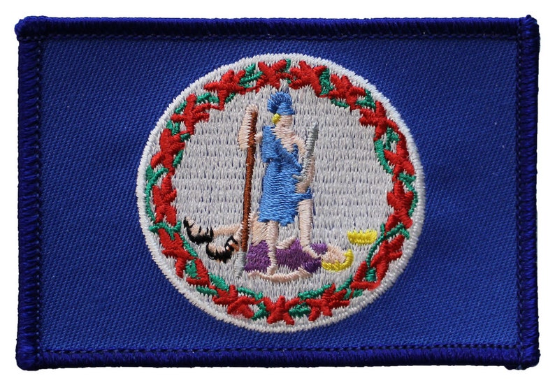 May include: A blue embroidered patch featuring the state seal of Virginia. The seal depicts a woman standing on a purple rock, holding a spear and a rifle, with a man lying at her feet. The seal is surrounded by a wreath of red and green leaves.