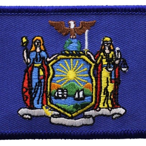 May include: Embroidered patch featuring the state seal of New York. The seal depicts a blue shield with a sun rising over a river and mountains. Two figures stand on either side of the shield, one holding a sword and the other holding scales of justice. The patch is surrounded by a blue border.
