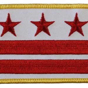 May include: A white patch with three red stars and two red stripes, surrounded by a gold border. The patch is a representation of the flag of Washington, D.C.