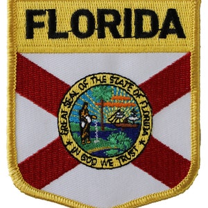 May include: A yellow and gold embroidered patch with the word "FLORIDA" in black lettering at the top. The patch features the state flag of Florida with a red cross on a white background and the state seal in the center.
