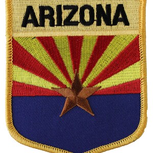 May include: Embroidered patch featuring the Arizona state flag. The flag is a red and yellow sunburst with a copper-colored star on a blue background. The patch is surrounded by a gold border and has the word "ARIZONA" stitched in black at the top.