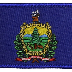 May include: A blue embroidered patch with the state seal of Vermont. The seal features a green pine tree, mountains, and a deer. The words "Vermont" and "Unity" are on a red ribbon.
