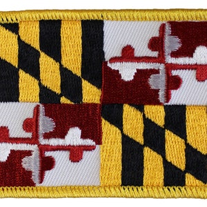May include: Embroidered patch featuring the Maryland state flag. The flag is a quartered design with a black and gold checkered pattern on the top left and bottom right quarters, and a white field with a red and white coat of arms on the top right and bottom left quarters.
