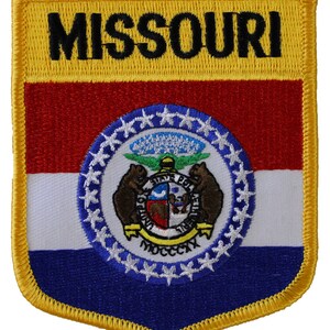 May include: An embroidered patch featuring the state flag of Missouri. The patch is yellow with a red, white, and blue flag in the center. The flag features the state seal with a bear, a river, and the words "United We Stand" and "MDCCLXXVI". The words "MISSOURI" are embroidered in black at the top of the patch.