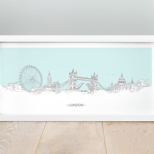 Peut inclure: Un dessin au trait noir et blanc de l'horizon de Londres, comprenant le London Eye, le Tower Bridge et la cathédrale Saint-Paul. L'horizon est sur un fond bleu clair et le texte "LONDON" est imprimé sous l'horizon.