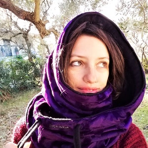 May include: A purple hooded neck warmer with a black drawstring. The neck warmer is made of a soft, plush fabric and has a quilted design.