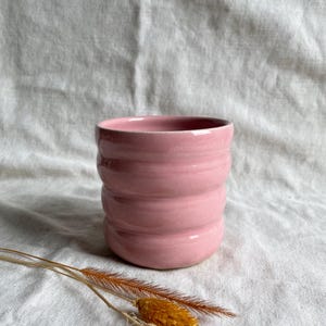 May include: A pink ceramic planter with a ridged design. The planter is sitting on a white fabric surface.