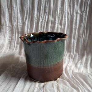 Könnte beinhalten: Eine handgefertigte Keramikvase mit gewelltem Rand. Die Vase ist zylindrisch, mit einem dunkelgrünen oberen Bereich, einem braunen Mittelteil und einem hellbraunen Sockel. Der Innenraum ist dunkelgrün glänzend.