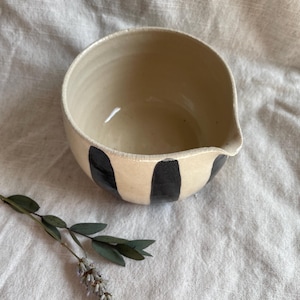 May include: A white ceramic mixing bowl with a black and white striped design. The bowl has a pouring spout on one side.