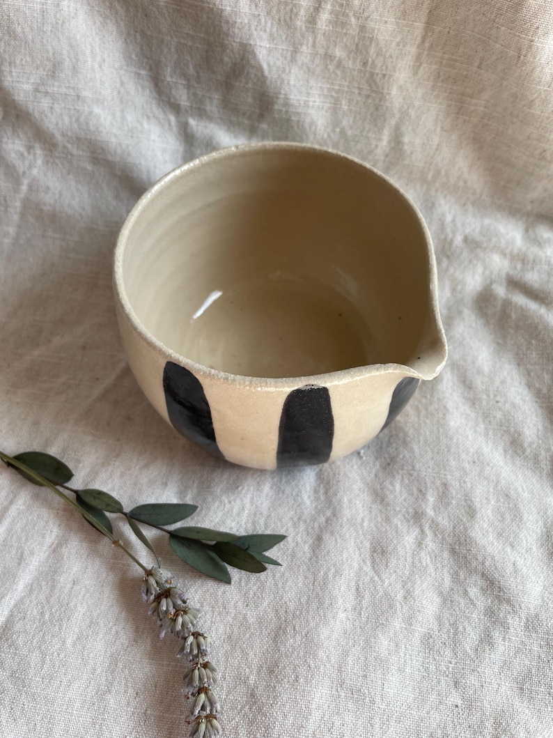 May include: A white ceramic mixing bowl with a black and white striped design. The bowl has a pouring spout on one side.