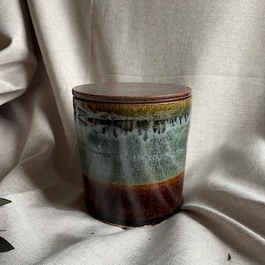 May include: A ceramic jar with a lid, featuring a brown, green, and blue glaze. The jar has a rounded shape and a smooth, glossy finish.