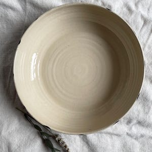 May include: A large, white ceramic bowl with a black rim. The bowl has a slightly textured surface and is empty.