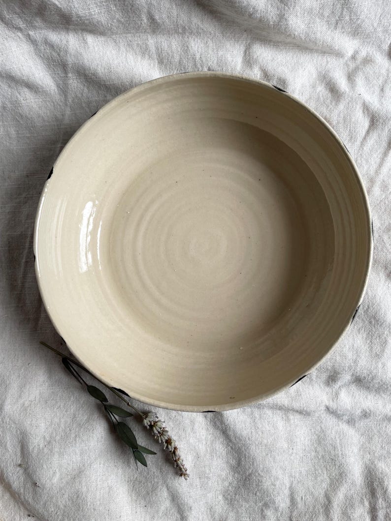 May include: A large, white ceramic bowl with a black rim. The bowl has a slightly textured surface and is empty.