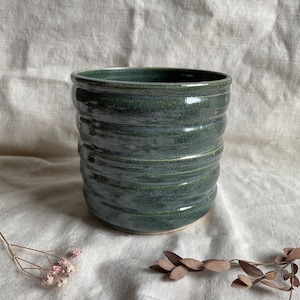 May include: A dark green ceramic planter with a textured, wavy design. The planter is made of pottery and has a smooth, glazed finish.
