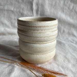 May include: A white ceramic mug with a textured, rippled design. The mug has a slightly off-white colour and a matte finish.
