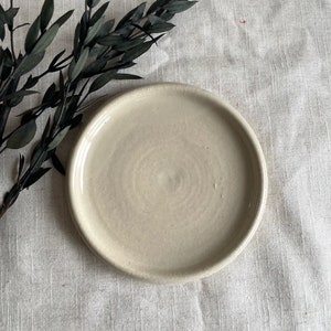 Puede incluir: Un plato de cer&aacute;mica blanco liso con un borde ligeramente elevado. El plato tiene un sutil patr&oacute;n de remolino en la superficie.