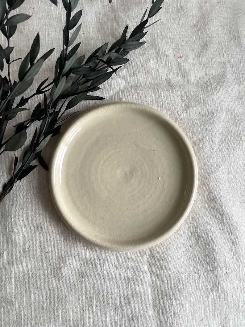 Puede incluir: Un plato de cer&aacute;mica blanco liso con un borde ligeramente elevado. El plato tiene un sutil patr&oacute;n de remolino en la superficie.