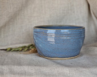 May include: A blue ceramic bowl with a slightly textured surface. The bowl is round and has a wide rim.