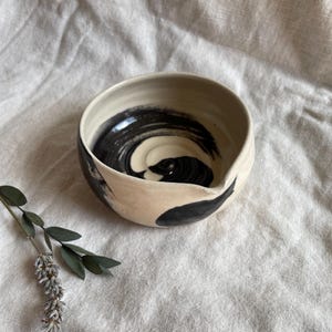 May include: A white ceramic bowl with a black swirl design. The bowl has a pour spout on one side.