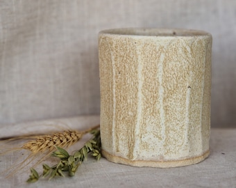May include: A white ceramic mug with a textured, striped design. The mug has a slightly off-white color and a rounded shape.