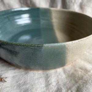 May include: A large, ceramic bowl with a light blue and white glaze. The bowl has a rounded shape and a wide rim.
