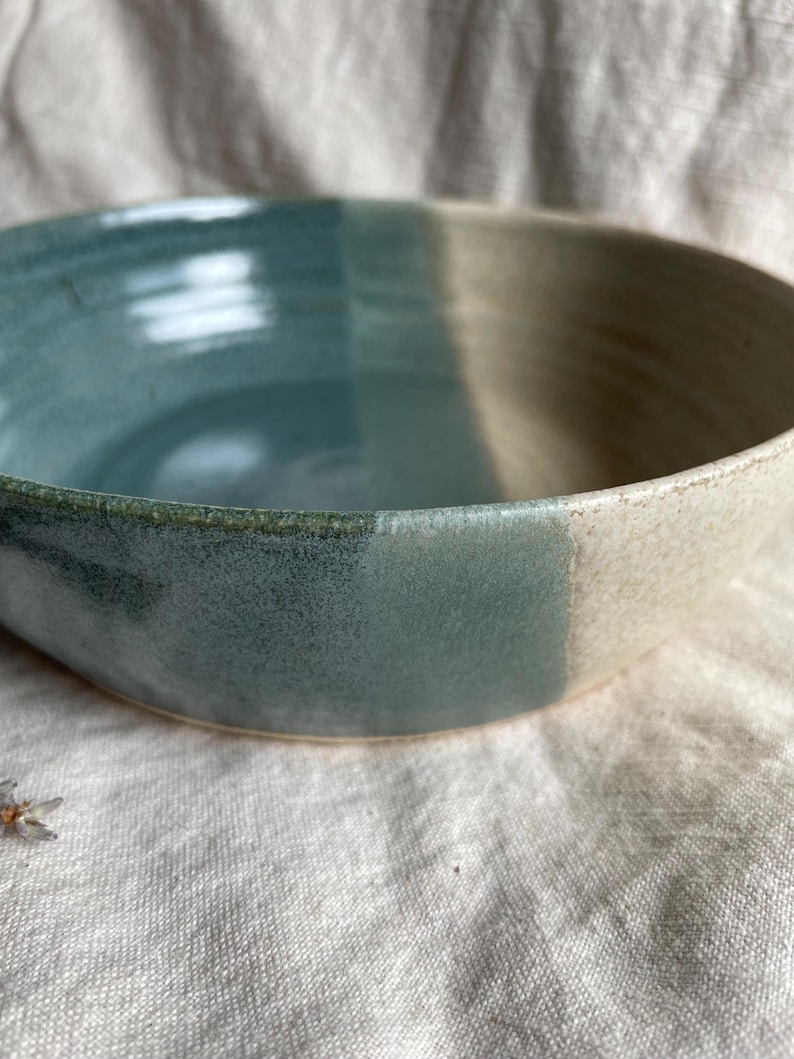 May include: A large, ceramic bowl with a light blue and white glaze. The bowl has a rounded shape and a wide rim.