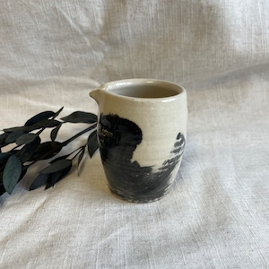 Peut inclure: Un petit pot à crème en céramique blanche avec un motif abstrait noir et blanc. Le pot à crème a un bec verseur et une anse.