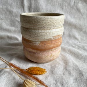May include: A white and orange ceramic mug with a textured surface. The mug has a rounded shape and a wide rim.