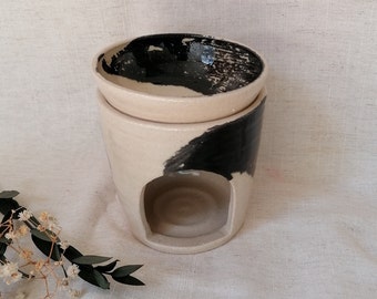 May include: A white ceramic oil diffuser with a black abstract design. The diffuser has a removable top bowl for essential oils and a lower section with an opening for a tea light.