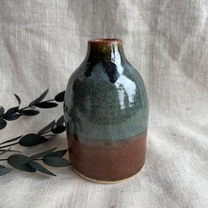 May include: A small, ceramic vase with a brown, green and blue glaze. The vase has a rounded body and a narrow neck.