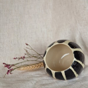 May include: A black and white ceramic vase with a round shape and a wide opening. The vase has a striped pattern with black stripes on a white background.