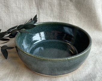 May include: A dark green ceramic bowl with a speckled glaze. The bowl has a slightly rounded rim and a smooth, glossy finish.