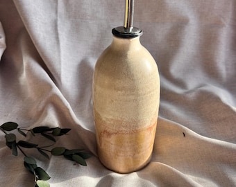 May include: A ceramic olive oil bottle with a stainless steel pour spout. The bottle has a light brown glaze with a darker brown band around the middle.