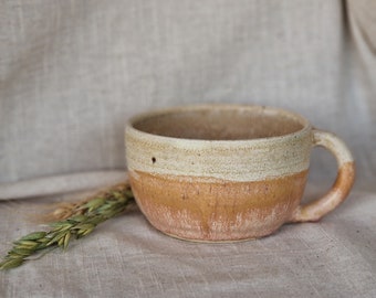 May include: A handmade ceramic mug with a white and brown glaze. The mug has a rounded shape and a handle.