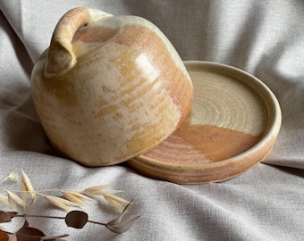May include: A ceramic butter dish with a lid and a handle. The dish is glazed in a light brown and cream color with a speckled finish.