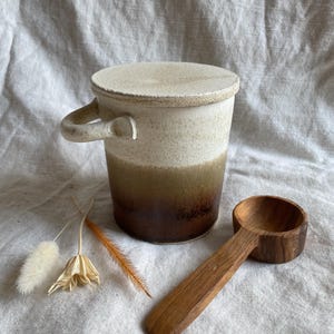 Peut inclure: Un pot en céramique blanche avec un couvercle et une cuillère en bois brun. Le pot est recouvert d'un glaçage brun, vert et blanc. La cuillère est en bois et a une finition naturelle.