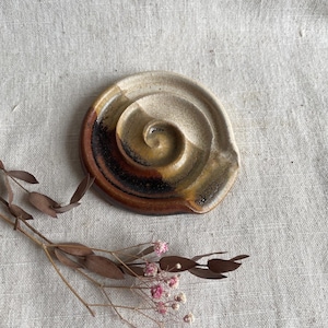 May include: A white, brown and yellow ceramic dish with a spiral design. The dish is slightly tilted and has a rough, textured surface.