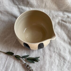 May include: A white ceramic bowl with a black and white striped design. The bowl has a pouring spout on one side.
