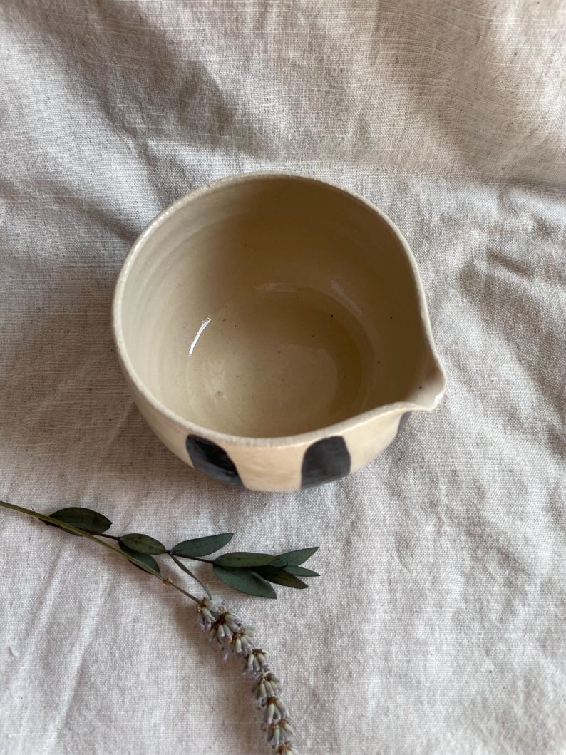 May include: A white ceramic bowl with a black and white striped design. The bowl has a pouring spout on one side.