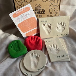 Könnte beinhalten: Ein Baby-Fußabdruck-Set mit Anleitung, roter, grüner und weißer Knete und drei weißen Keramikplatten mit dem Namen "Edward" und dem Datum "10.07.24" eingraviert.