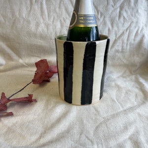 Könnte beinhalten: Ein schwarz-weiß gestreifter, keramischer Flaschenkühler mit einer Flasche Champagner darin. Das Flaschenetikett lautet "Methode Traditionnelle".