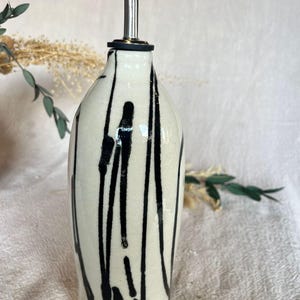 May include: A ceramic oil bottle with a black and white drip pattern. The bottle has a stainless steel spout with a black rubber stopper. The design is minimalist and modern, suitable for kitchen use.