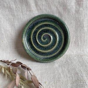 Könnte beinhalten: Eine kleine, runde Keramikschale mit grüner Glasur und einem Spiralmuster. Die Schale ist perfekt für die Aufbewahrung von kleinen Gegenständen wie Schmuck oder Schlüssel.