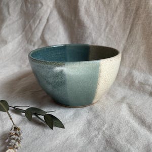 May include: A ceramic bowl with a light blue and white glaze. The bowl has a rounded shape and a wide rim.