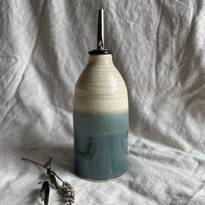May include: A ceramic olive oil bottle with a white and blue glaze. The bottle has a stainless steel pour spout.